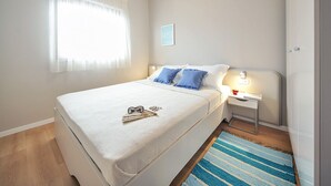 Ein Schlafzimmer mit Bett, Nachttisch, Lampe und einem Fenster mit Vorhängen.