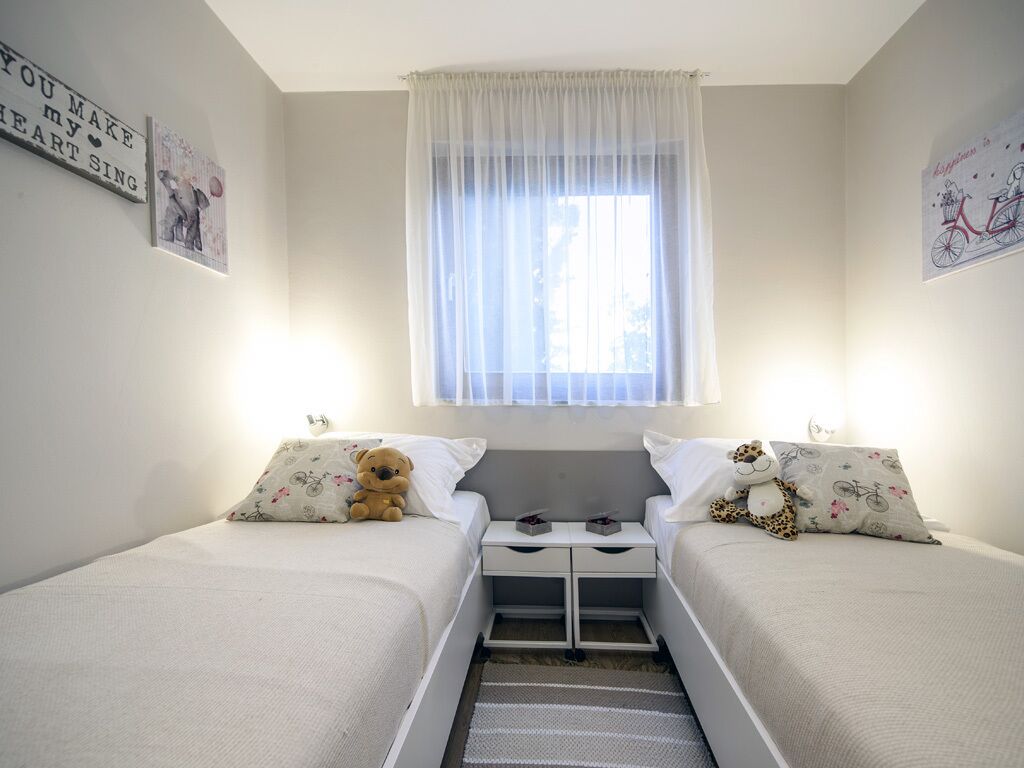 A twin bedroom with two beds, a window with sheer curtains, and wall art.