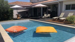 Une piscine équipée de deux coussins flottants, un espace patio avec des meubles d’extérieur et un coin salon abrité.