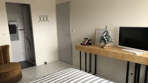 Un salon moderne avec un tapis à rayures, une table basse en bois sur laquelle est posée une petite plante, un téléviseur à écran plat et une porte sur laquelle est accrochée une serviette.