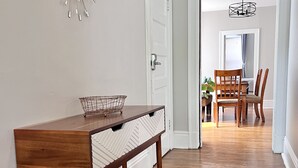 Un pasillo con una mesa y sillas de madera, un adorno en la pared y un área de comedor al fondo.