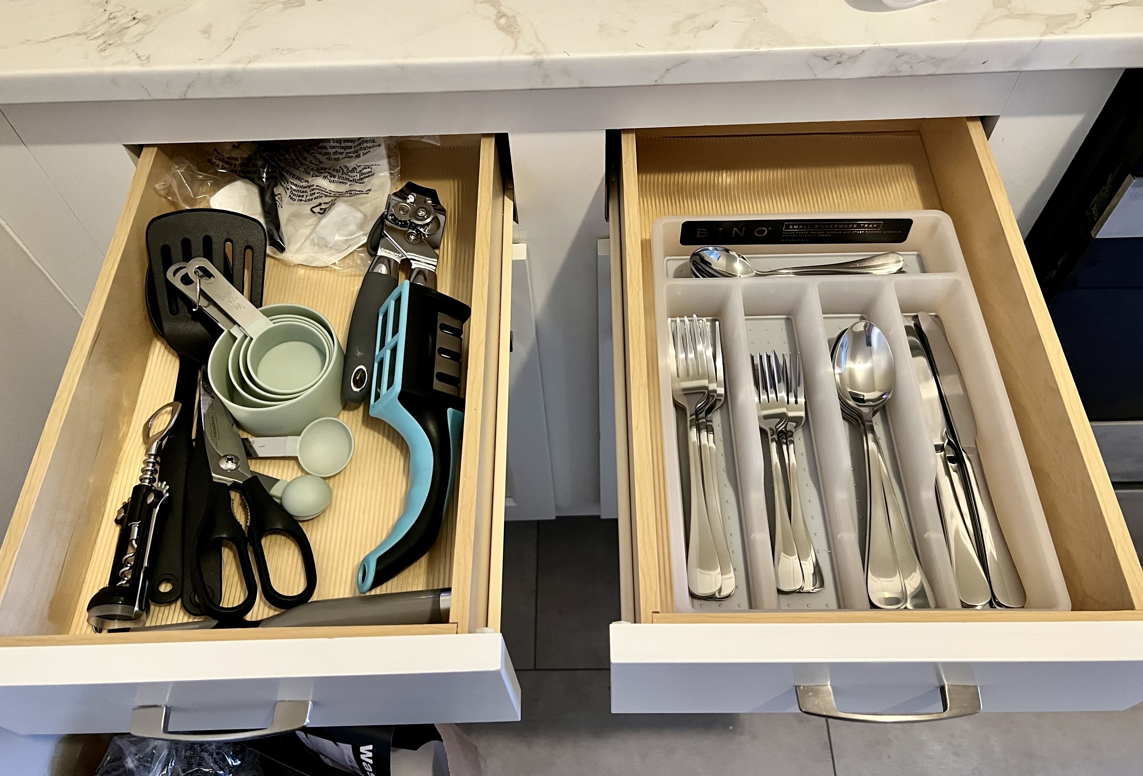 A drawer with kitchen utensils and a pair of scissors.