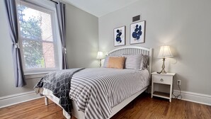 Un dormitorio con cama, mesitas de noche, lámpara y cuadros en la pared.