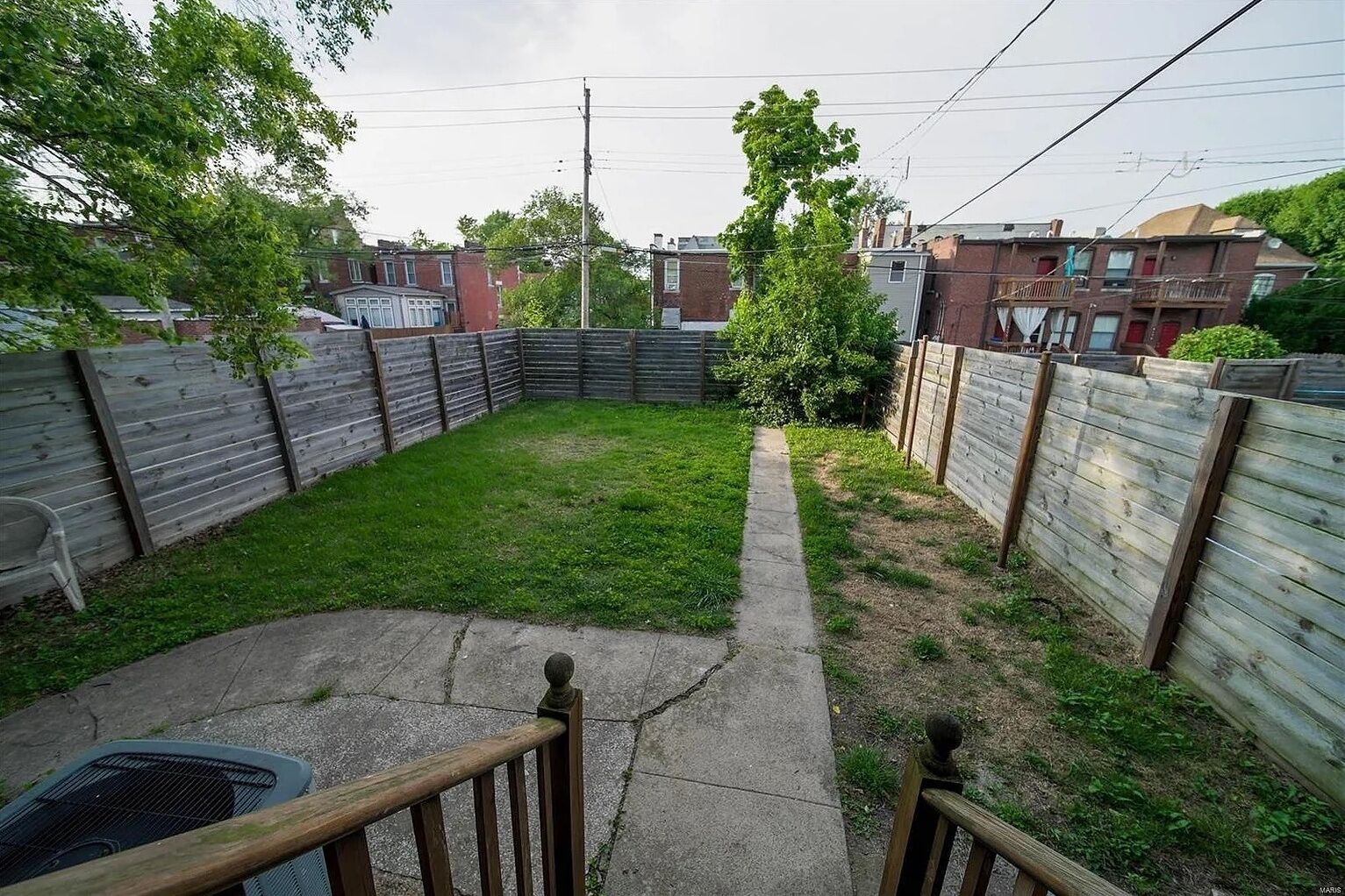 Un jardin avec une pelouse, un chemin en béton et des clôtures en bois.