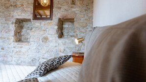 A bedroom with a stone wall, a bed with patterned pillows, a nightstand with a lamp, and a framed picture above the bed.