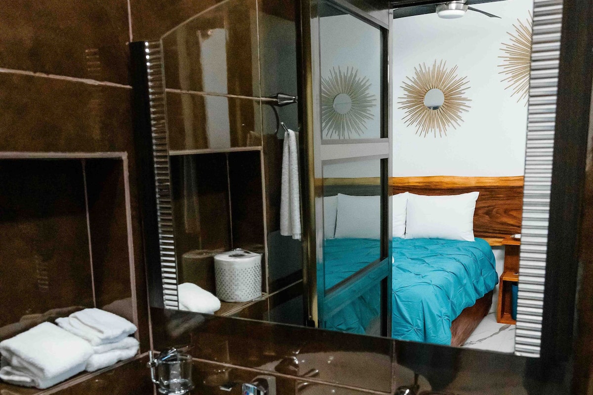 A bathroom with a white sink, a mirror, and a bed with a blue bedspread.