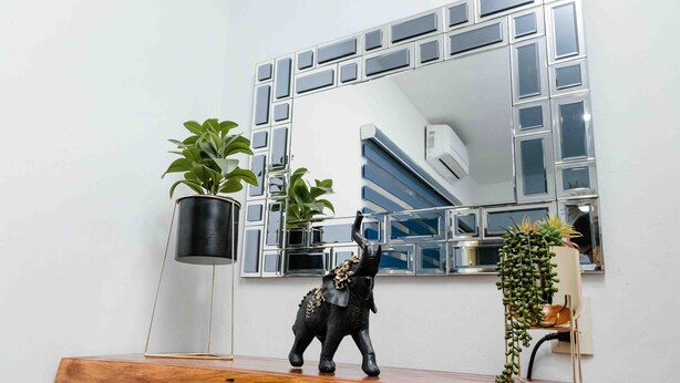 A wooden console table with a decorative elephant figurine, a potted plant, and a mirror with a geometric frame. - Hotel Naomi  (Bacalar)