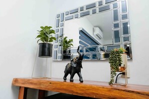 A wooden console table with a decorative elephant figurine, a potted plant, and a mirror with a geometric frame. - Hotel Naomi  (Bacalar)