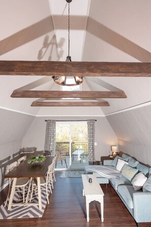 A spacious loft with a high ceiling, exposed wooden beams, a dining area with a table and chairs, a sofa, and a view through a large window. - Cheerful 3 Bedroom Swiss Chalet at Table Rock Lake (Lampe)