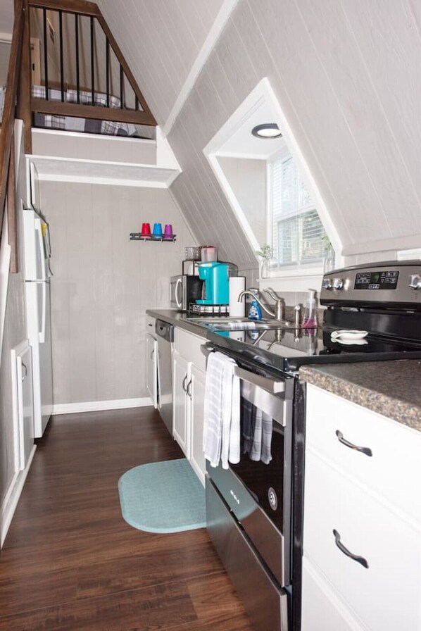 A modern kitchen with white cabinets, a stainless steel range, and a built-in oven. There is a wooden staircase leading to an upper level, and a window providing natural light.