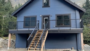 A two-story blue house with a balcony, a staircase, and a view of a forested mountain.