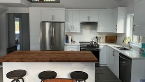 A modern kitchen with white cabinets, stainless steel appliances, and a wooden island with bar stools.