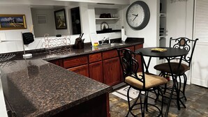 Une cuisine dotée de plans de travail en granit, de meubles en bois, d’un tabouret de bar noir et d’une horloge murale.