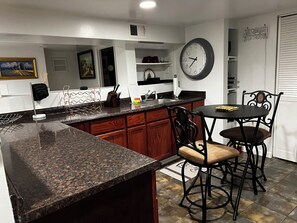 A kitchen with granite countertops, wooden cabinets, a black bar stool, and a wall clock.