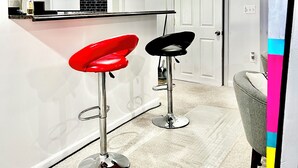 Une cuisine moderne avec des meubles blancs et un pare-feu noir, deux tabourets de bar et un fauteuil gris.
