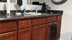 Une cuisine avec un meuble en bois, un évier, une machine à café et une horloge murale.