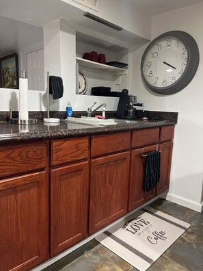A kitchen with a wooden cabinet, a sink, a coffee maker, and a wall clock.