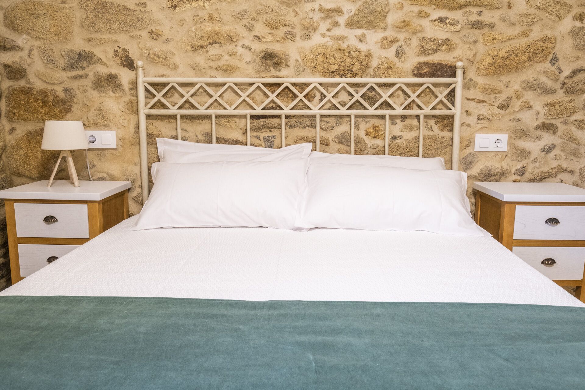 Una cama con cabecera blanca y dos mesitas de noche, cada una con una lámpara y un cajón.