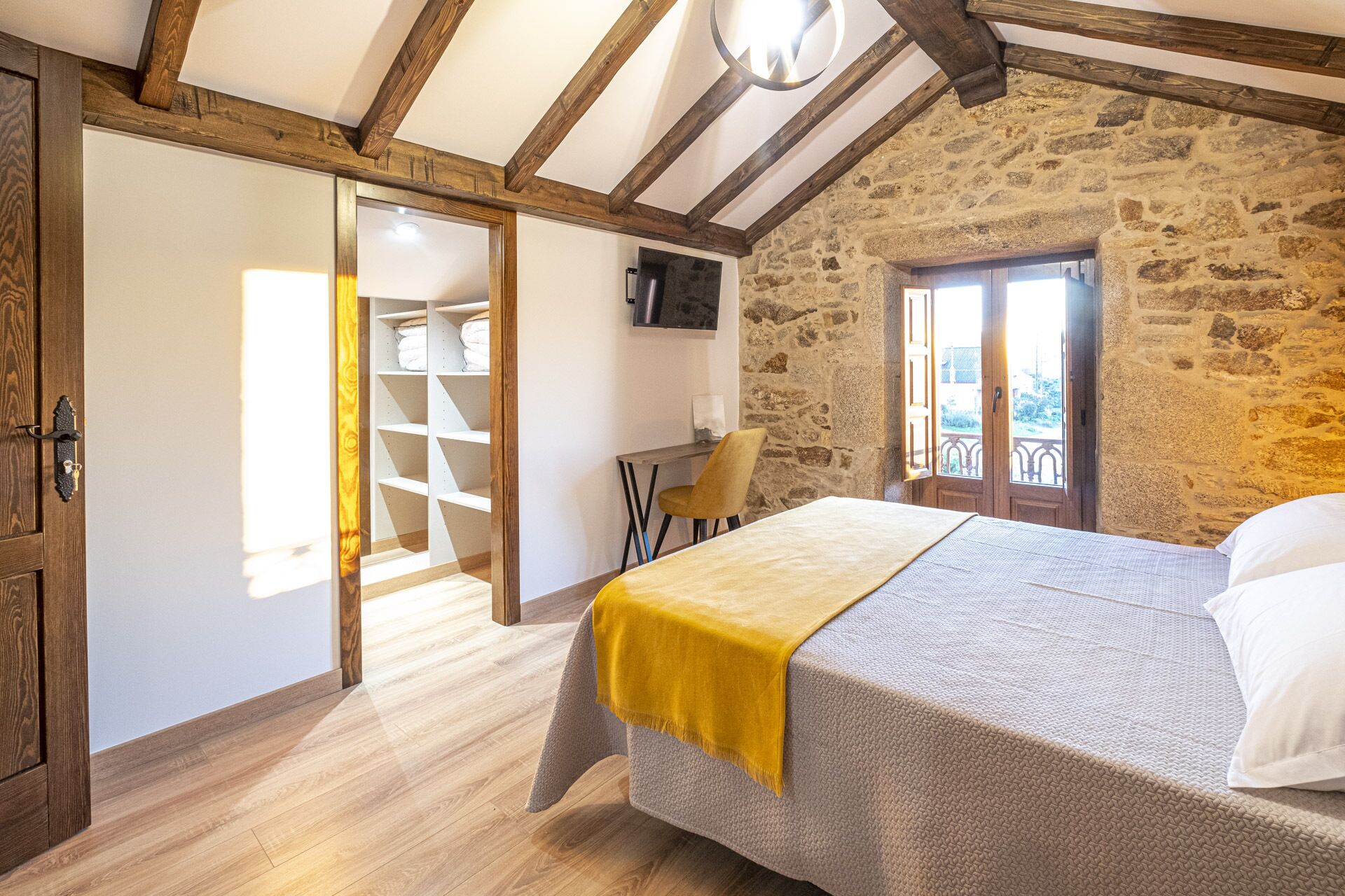 Un dormitorio con cama, una silla, un escritorio, un armario y una pared de piedra.