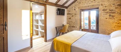 Un dormitorio con cama, una silla, un escritorio, un armario y una pared de piedra.