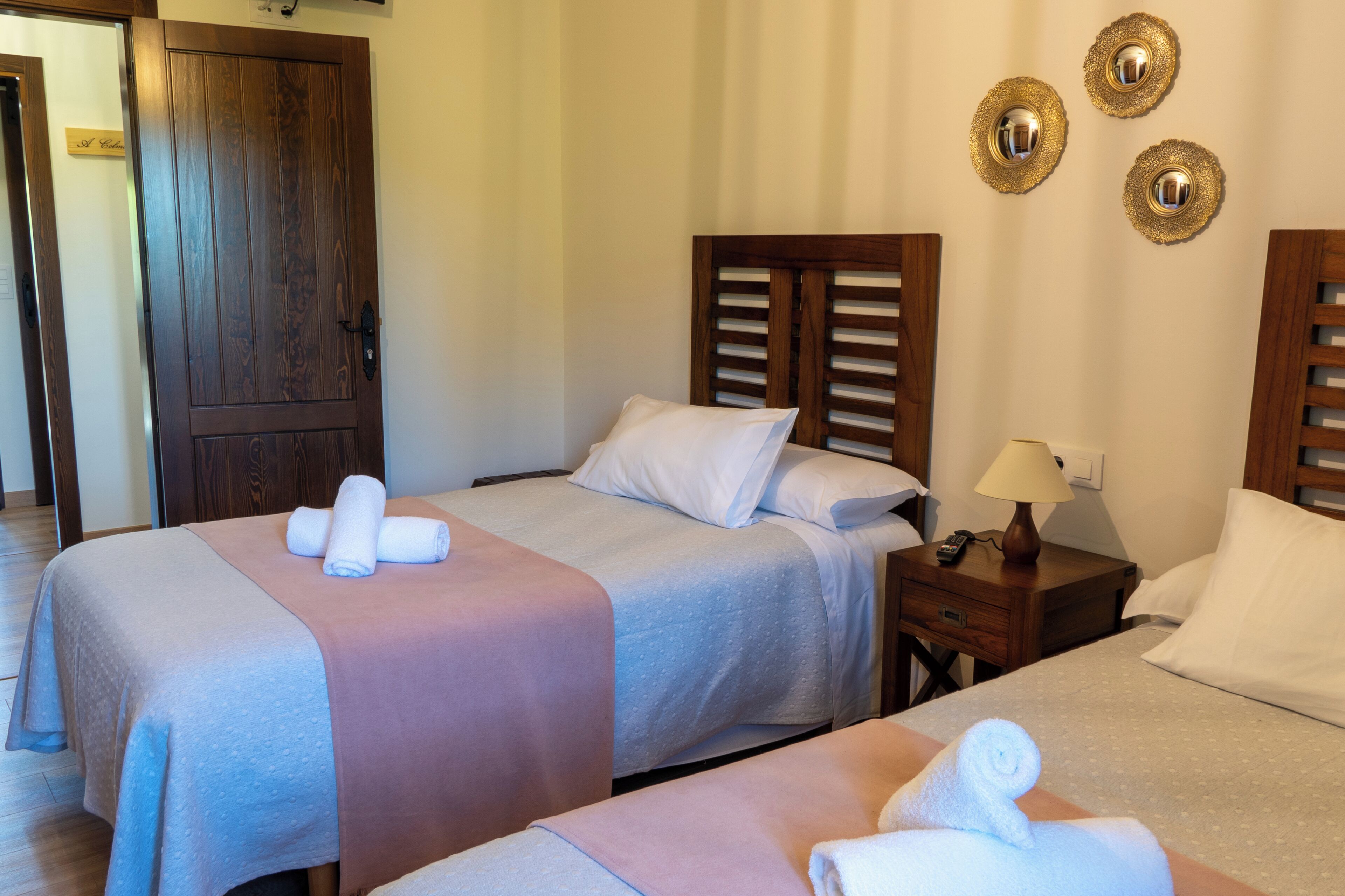 A hotel room with two beds, a wooden door, a nightstand with a lamp, and three wall-mounted decorative items.