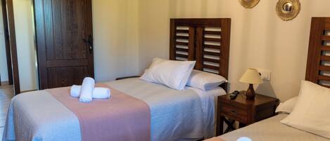 A hotel room with two beds, a wooden door, a nightstand with a lamp, and three wall-mounted decorative items.