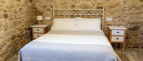 A bed with a white headboard, two bedside tables, and a stone wall backdrop.