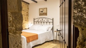 Een slaapkamer met een stenen muur, een bed met witte beddengoed, een houten vloer en een schilderij aan de muur.