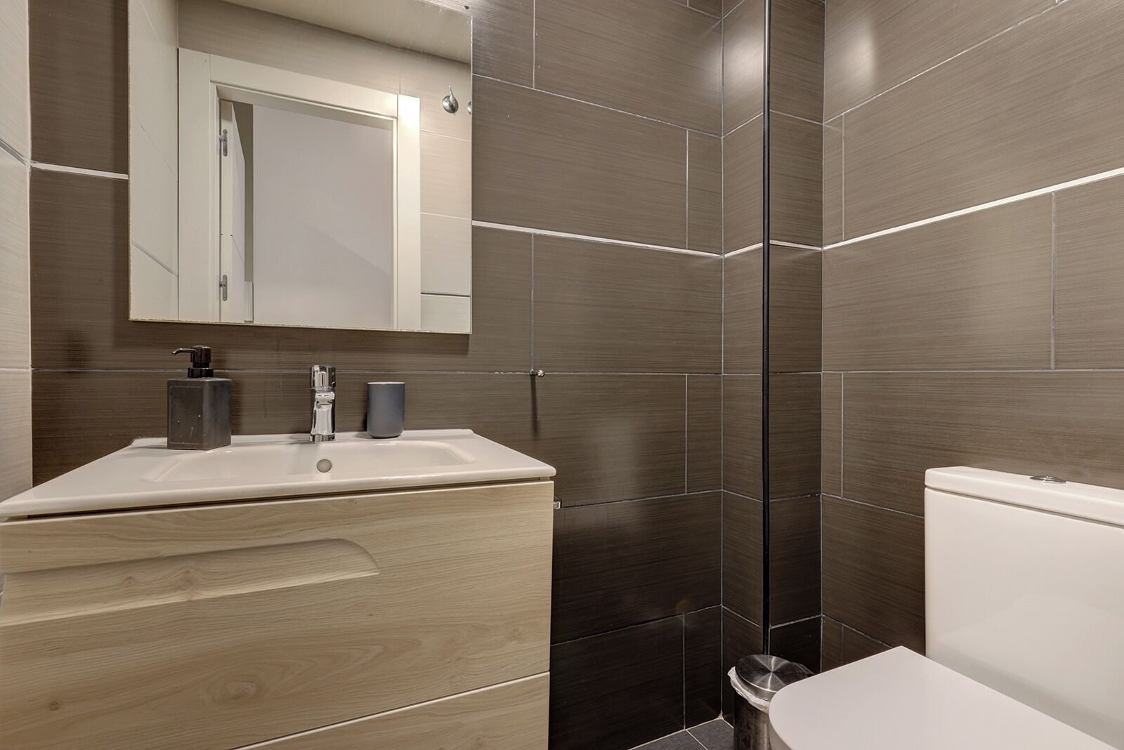 A modern bathroom with a wooden vanity, a sink, a mirror, and a toilet.