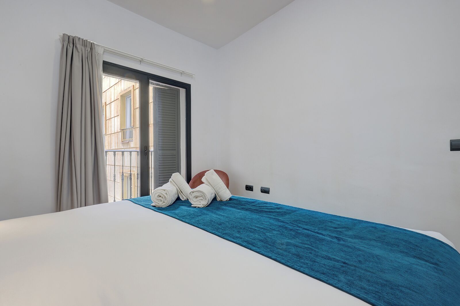 Een slaapkamer met een bed, een blauwe deken en twee opgerolde handdoeken op het bed.