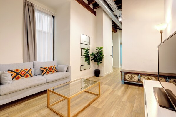 Un salon moderne avec un canapé, une table basse en verre, une plante en pot et un téléviseur.