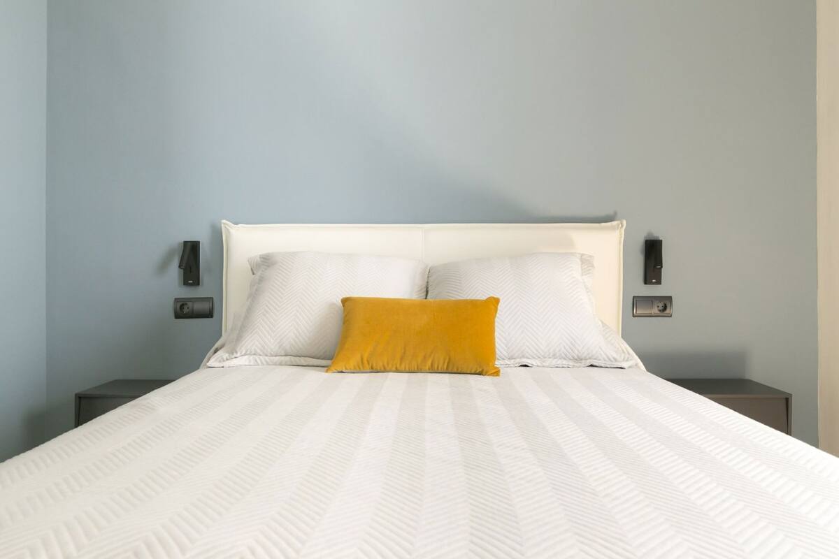 Un lit avec une tête de lit blanche, deux oreillers et un seul coussin jaune, utilisé comme élément décoratif.
