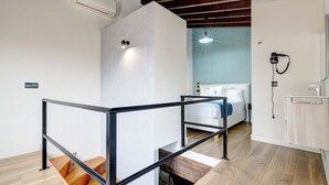 A modern hotel room with a wooden staircase, a bed with a blue accent, and a small bathroom with a sink and mirror. - Heredia Suites Centro (Málaga)