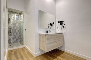 Une salle de bain avec une douche, un meuble-lavabo avec un miroir et un sèche-cheveux fixé au mur.