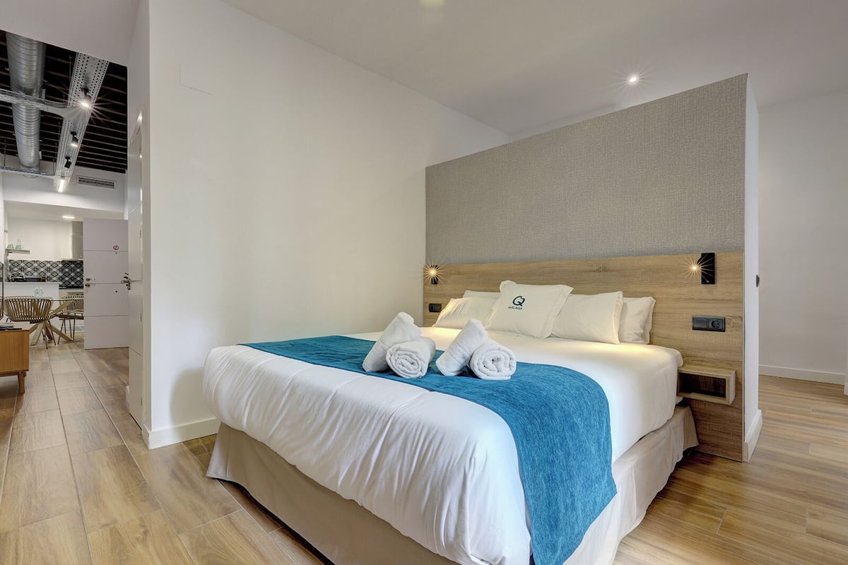 Une chambre d’hôtel moderne avec un grand lit, une tête de lit en bois et une vue sur la cuisine.