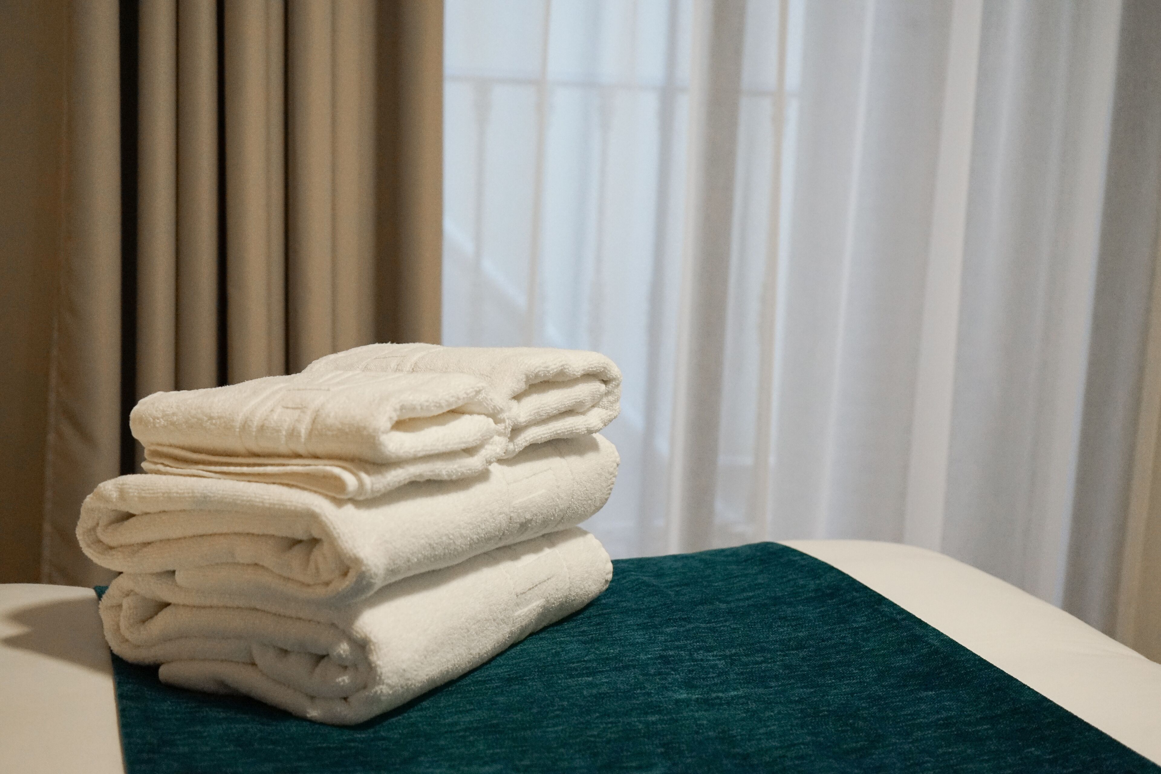 A stack of folded towels on a bed with a green bedspread.