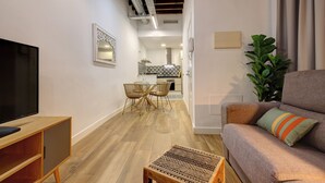 A modern living room with a flat-screen TV, a sofa with cushions, a coffee table, and a dining area with chairs. - Heredia Suites Centro (Málaga)