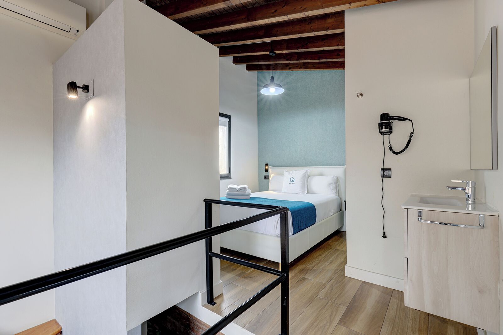 Ein modernes Hotelzimmer mit einem Bett, einem Badezimmer mit Waschbecken und Spiegel sowie einer Treppe.