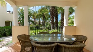 A covered outdoor dining area with a glass table and wicker chairs, surrounded by palm trees and a garden. - Wide 3 bedrooms apartment wifi, air conditioning, garage (Alto do Semino, Quarteira)