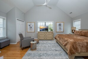 Quarto com cama grande, escrivaninha, cadeira e ventilador de teto.