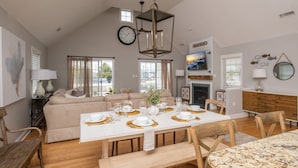 A spacious living area with a high ceiling, a dining table set for six, and a cozy seating arrangement.