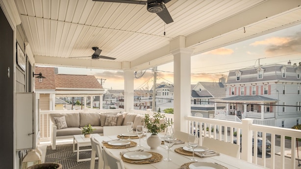 A covered balcony with a dining table set for four, a sofa, and a potted plant.