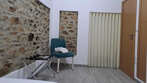 Una habitación pequeña y acogedora con pared de piedra, un sillón azul y toallas, una puerta de madera y suelo de madera.