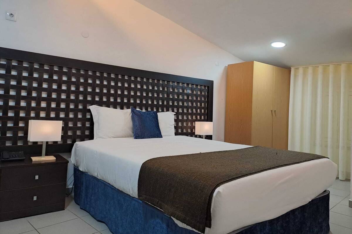 Ein Hotelzimmer mit einem großen Bett, zwei Nachttischen, einem Kleiderschrank und einem Vorhang.