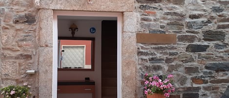 A stone building entrance with a wooden bench, a door, and a wall-mounted light fixture.