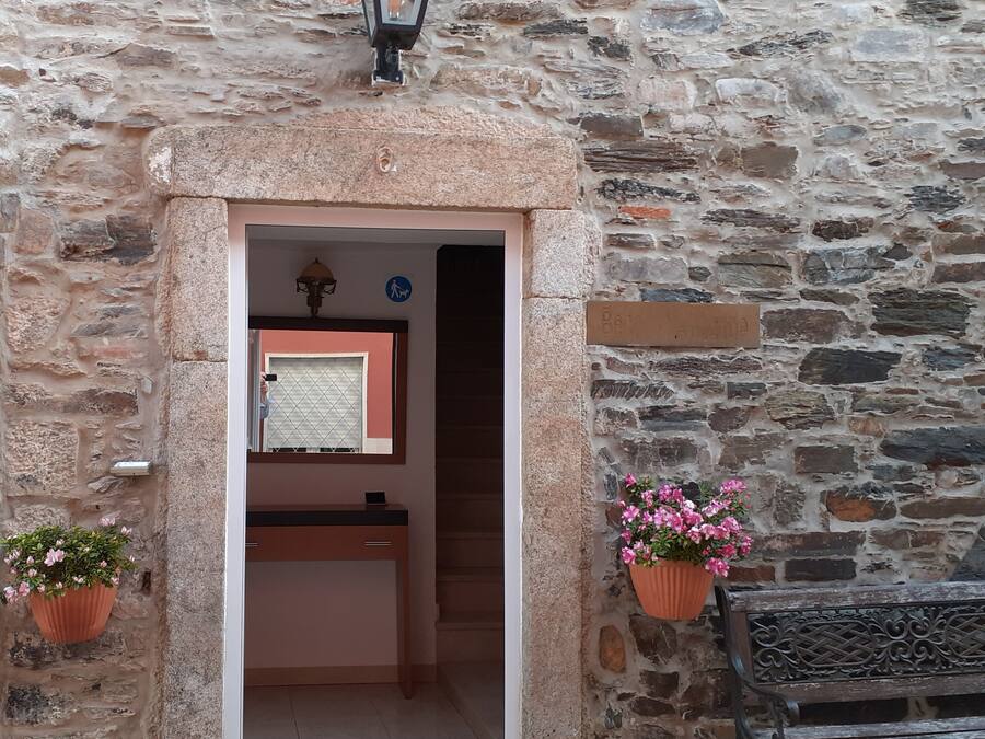 Entrada de um edifício de pedra com um banco de madeira, uma porta e um candeeiro fixado na parede.