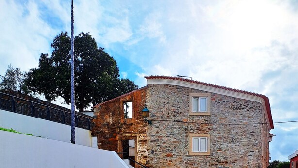 Un edificio de piedra con una escalera que lleva a una puerta, una pared blanca y un camino de grava.
