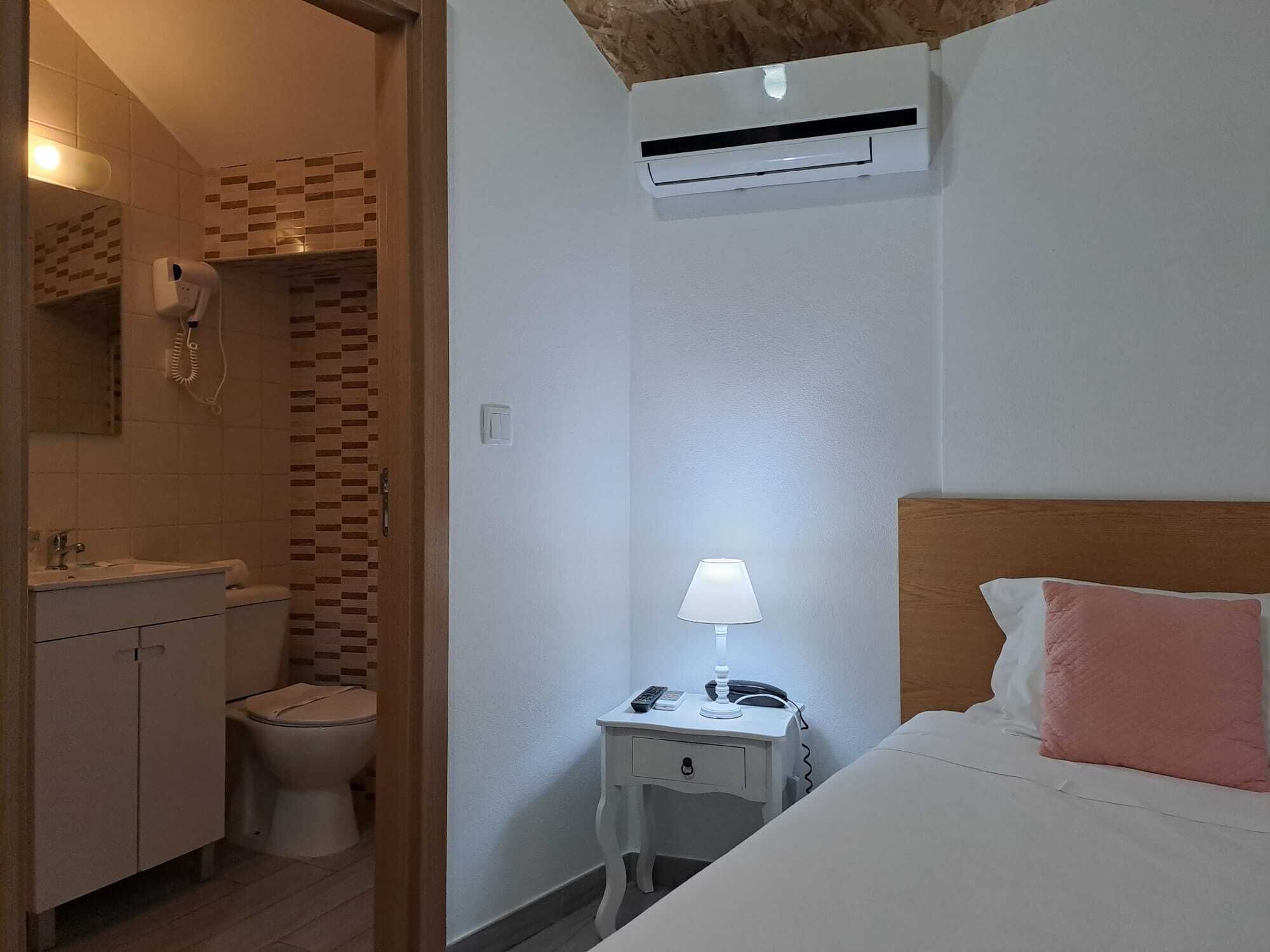 A hotel room with a bed, bedside table, lamp, and an air conditioning unit.