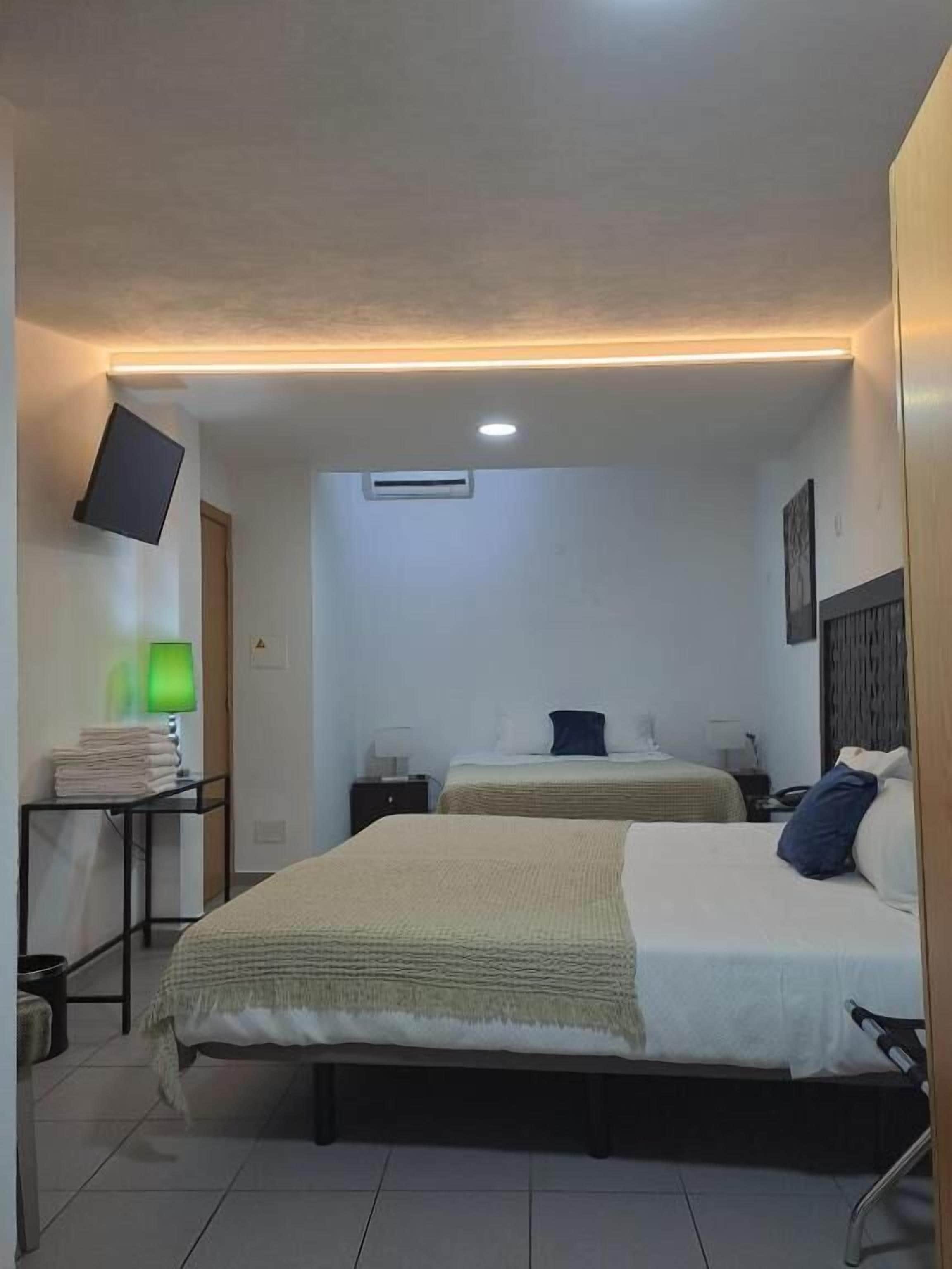 Een hotelkamer met twee bedden, een flatscreen televisie, een airconditioning en een nachtkastje met een lamp.