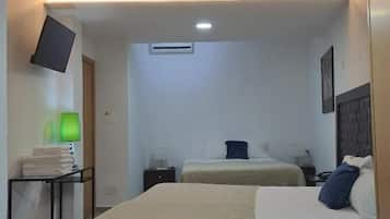 A hotel room with two beds, a flat-screen TV, an air conditioning unit, and a bedside table with a lamp.